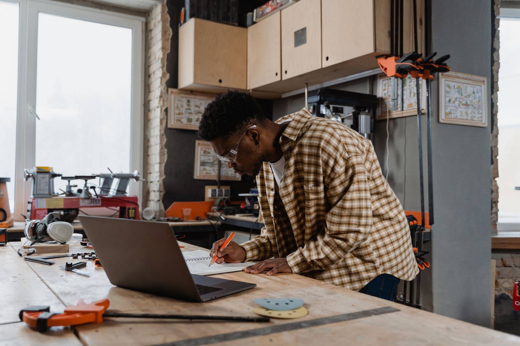 A man writing notes beside his laptop at a workshop bench