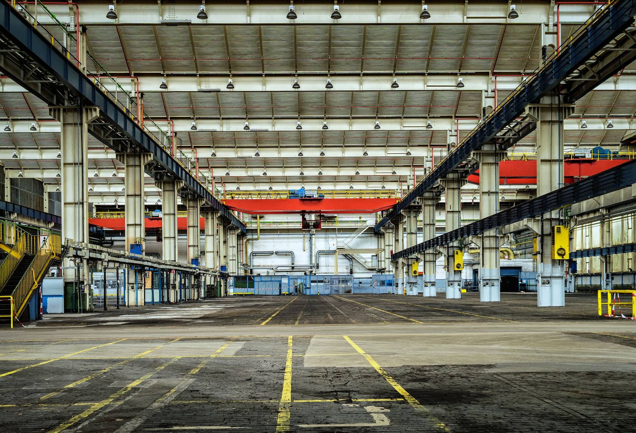 A wide, empty factory hall with overhead cranes and painted floor markings