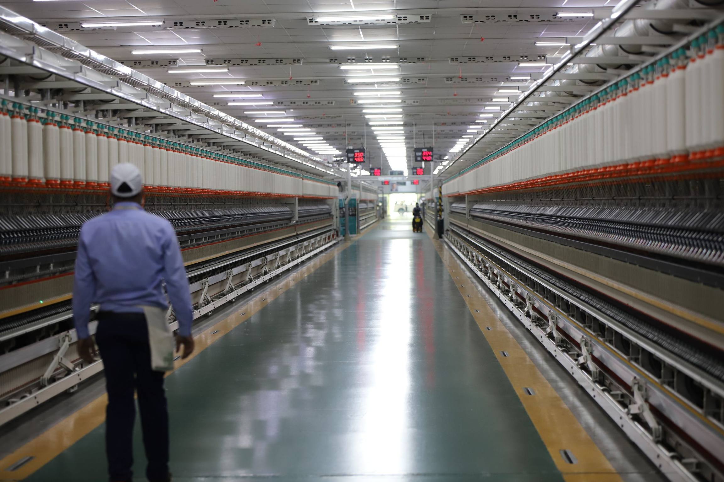 A man walking down a long, brightly lit aisle between rows of production machines